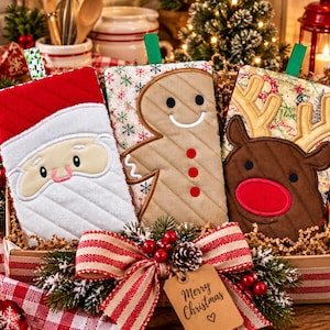 Puede incluir: Tres manoplas de horno rectangulares acolchadas con diseños navideños: una cara de Papá Noel, un hombre de jengibre y un reno con grandes astas. Cada manopla tiene un lazo de tela verde y se presenta en una caja de regalo con un lazo.