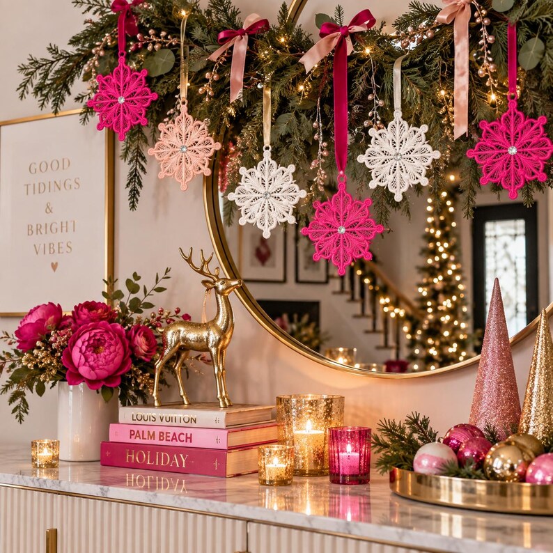 May include: A collection of hanging lace snowflake ornaments in shades of hot pink, light pink, and white, each featuring a central rhinestone. The ornaments are suspended by ribbons from a green garland draped over a large round mirror.