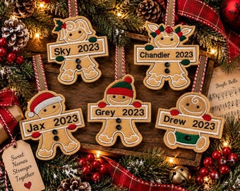May include: Five tan gingerbread person ornaments with embroidered details, each holding a rectangular sign with a name and the year 2023. The ornaments feature various accessories like hats and scarves, and are suspended by red and white striped ribbons.
