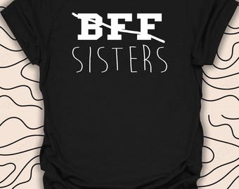 Puede incluir: Camiseta negra con texto blanco que dice "BFF" con una línea tachada y "SISTERS" debajo.
