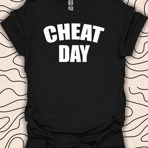 Może przedstawiać: Czarny T-shirt z białym napisem "CHEAT DAY".