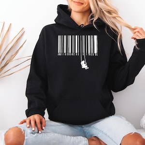 Könnte beinhalten: Schwarzer Kapuzenpullover mit einem weißen Aufdruck eines Kindes auf einer Schaukel und einem Barcode-Design. Der Pullover hat eine Vordertasche und eine Kapuze mit Kordelzug. Der Text und der Barcode sind weiß.
