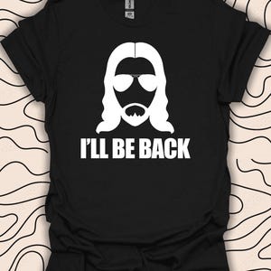 May include: Black t-shirt featuring a white silhouette of a person with long hair and sunglasses. The text "I'll be back" is printed below the silhouette.