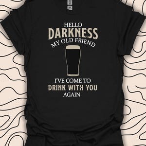May include: Black t-shirt with white text that reads "Hello Darkness My Old Friend I've Come To Drink With You Again". A glass of dark beer is pictured in the centre of the text.