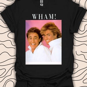 May include: Black t-shirt with a white graphic of the band Wham! featuring George Michael and Andrew Ridgeley.