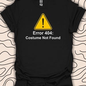 Può includere: Maglietta nera con un cartello di avvertimento giallo e il testo "Errore 404: Costume non trovato".