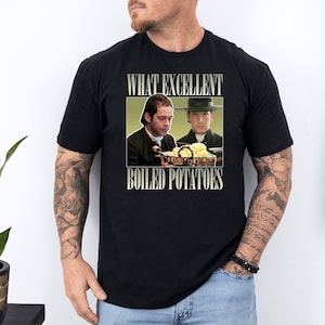 Puede incluir: Camiseta negra con un gráfico de dos hombres y el texto "WHAT EXCELLENT BOILED POTATOES". El gráfico está en un marco rectangular con un fondo verde. La camiseta está hecha de un material suave.