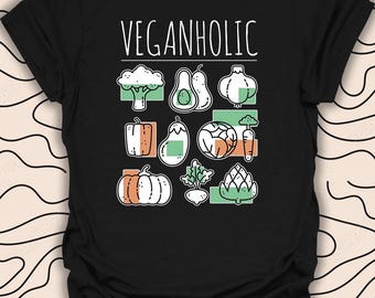 May include: Black t-shirt with the text "VEGANHOLIC" in white. The shirt features a graphic of various vegetables, including broccoli, avocado, garlic, pumpkin, and artichoke.