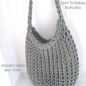 May include: A gray double-sided rope bag tote. The bag is made of thick rope and has a simple, minimalist design. The text "EASY TUTORIAL ROPE BAG" is at the top of the image and the text "DOUBLE SIDED BAG TOTE" is at the bottom of the image.