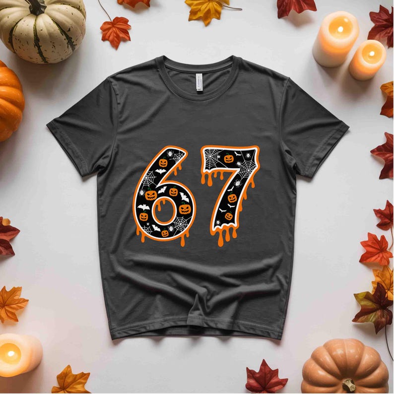 May include: Dark gray t-shirt with a Halloween-themed design. The number "67" is displayed in orange, black, and white, featuring pumpkins, bats, and spiderwebs. The design has a dripping effect.