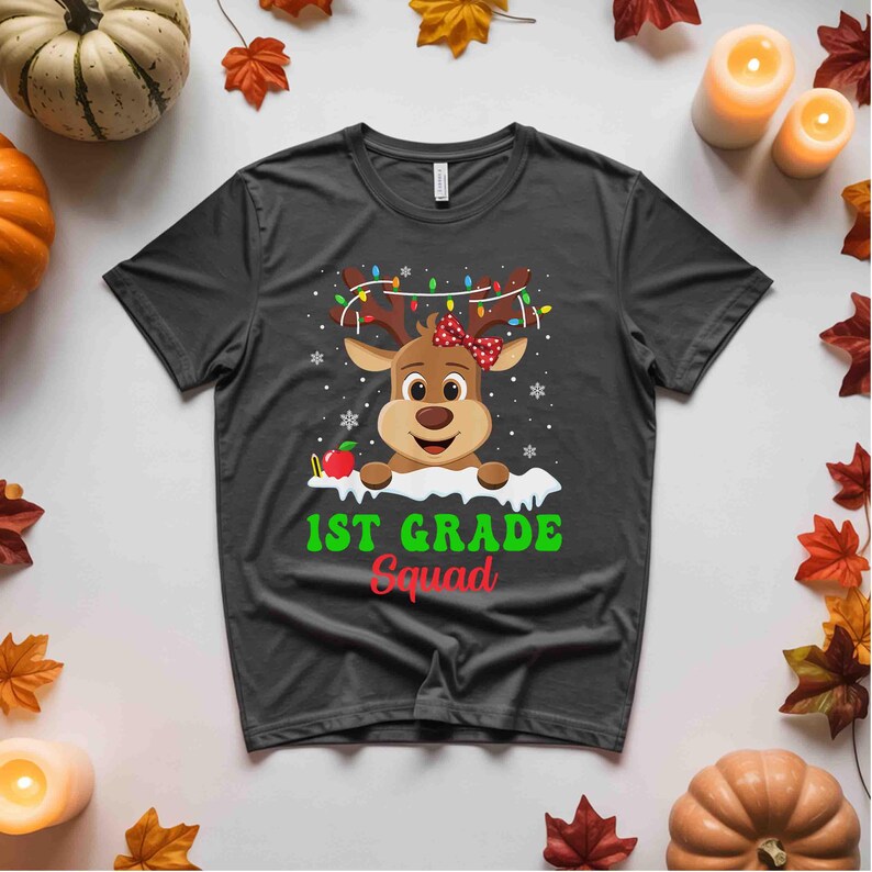 May include: A dark gray t-shirt featuring a cartoon reindeer with antlers adorned with Christmas lights and a red bow. The text "1ST GRADE Squad" is printed in green and red below the reindeer.