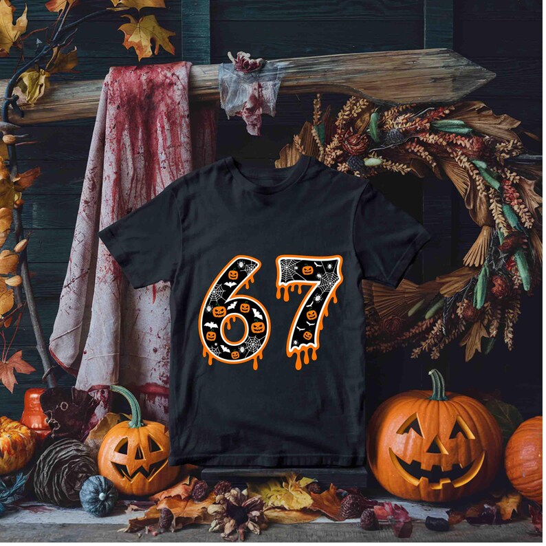 May include: Black t-shirt with the number 67 in orange and white, decorated with bats, pumpkins, and spiderwebs. The number has a dripping effect. The shirt is displayed with carved pumpkins and autumn foliage.
