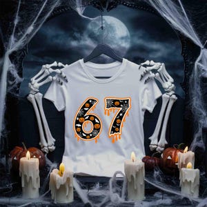 May include: White t-shirt with the number "67" in a Halloween-themed design. The numbers are black with orange dripping accents, bats, and jack-o'-lanterns. The shirt is hanging on a black hanger, with a spooky background.