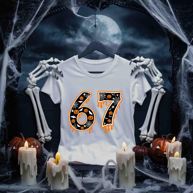 May include: White t-shirt with the number "67" in a Halloween-themed design. The numbers are black with orange dripping accents, bats, and jack-o'-lanterns. The shirt is hanging on a black hanger, with a spooky background.