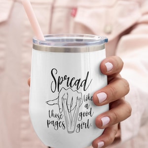 May include: White insulated wine tumbler with a clear lid and a pink straw. The tumbler features the text "Spread like those pages like a good girl" in black script, with a graphic of a hand and a book.