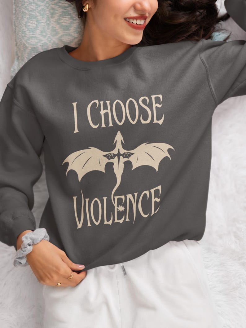 Woman wearing a comfy white, unisex crewneck sweatshirt. Striking graphic design on the front features a majestic Black Dragon, boldly proclaiming the phrase I Chose Violence, a statement that's sure to resonate with fans of intense, passionate relationships.