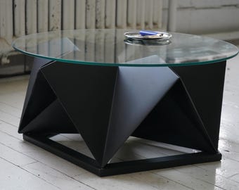 Könnte beinhalten: Ein schwarzer geometrischer Couchtisch mit einer Glasplatte. Der Tisch hat ein einzigartiges, von Origami inspiriertes Design und eine sechseckige Basis.