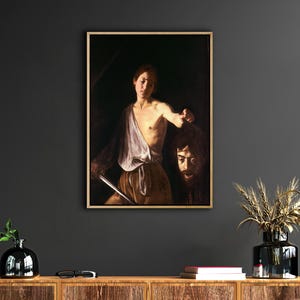 May include: A painting of a young person holding a sword and a severed head. The person is wearing a white tunic and the head is covered in a dark cloth. The painting is set against a dark background.