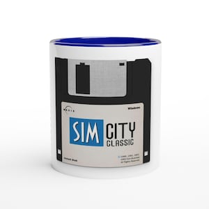 May include: White ceramic mug with a blue interior featuring a design of a black floppy disk with the text "SIM CITY CLASSIC" in blue and white. The mug also includes the Maxis logo and the text "Install Disk".