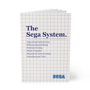May include: A white instruction manual titled "The Sega System" with a blue grid pattern. The cover includes the Sega logo and text in multiple languages: Operating Instructions, Bedienungsanleitung, Bruksanvisning, Mode d'emploi, Manual de instrucciones, and Istruzioni per l'uso.