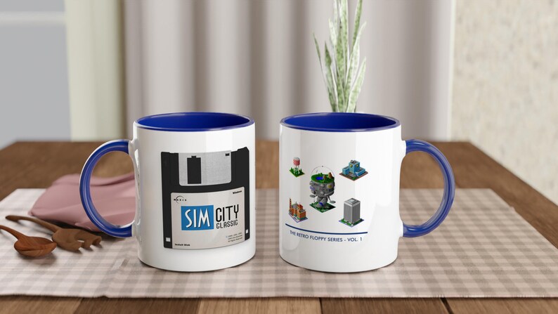 May include: Two white ceramic mugs with blue interiors and handles. One mug features a floppy disk graphic with "SIM CITY CLASSIC" text. The other mug displays retro game graphics and the text "THE RETRO FLOPPY SERIES - VOL. 1."