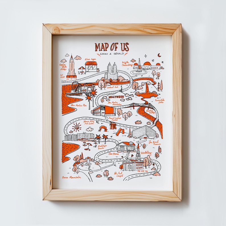 Może przedstawiać: Oprawiony wydruk artystyczny zatytułowany "Map of Us" w stylu ręcznie rysowanym. Mapa zawiera pomarańczowe i czarne ilustracje zabytk&oacute;w i lokalizacji, z nazwiskami "Sarah & Gerald" na g&oacute;rze. Rama wykonana jest z jasnego drewna.