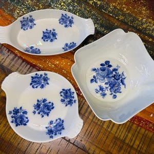 Könnte beinhalten: Drei weiße Porzellan-Servierschalen mit blauen Blumenmustern. Die Schalen sind oval, rund und quadratisch und weisen jeweils ein anderes Design aus blauen Rosen auf. Die Schalen haben Griffe und einen gewellten Rand.