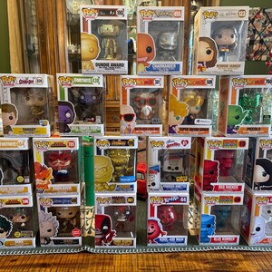 Puede incluir: Una colección de figuras de vinilo Funko Pop! en sus cajas originales. Las figuras presentan personajes de varias franquicias, incluyendo Fortnite, Pokémon y Harry Potter. Las figuras se exhiben sobre una superficie de madera.
