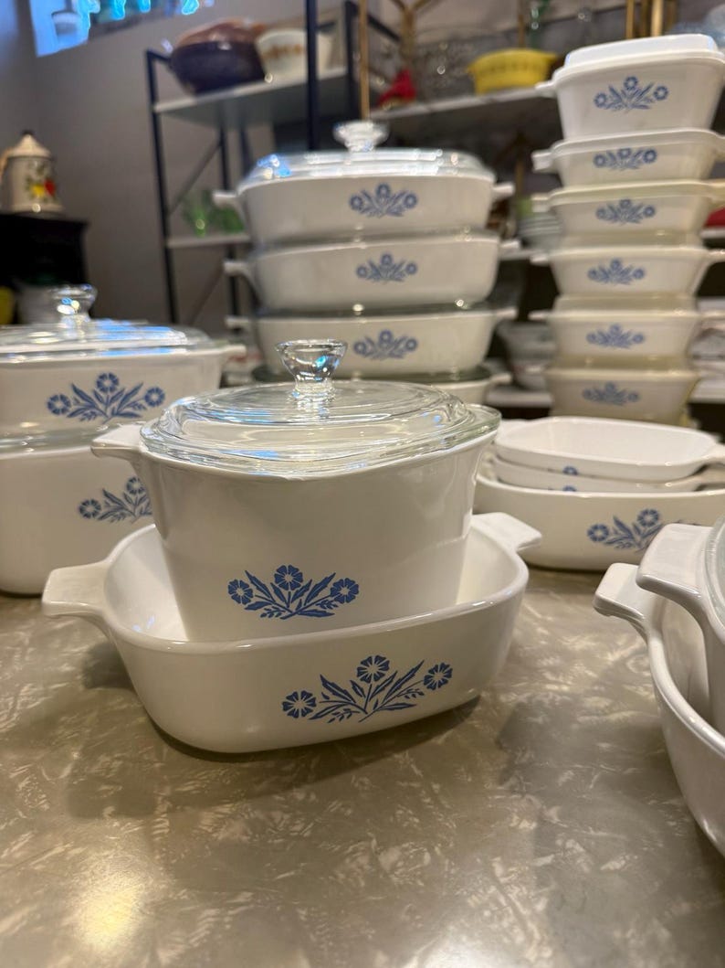 May include: A collection of white glass bakeware featuring a blue floral pattern. The set includes various rectangular and square casserole dishes with integrated handles and clear glass lids, showcasing a consistent design across all pieces.