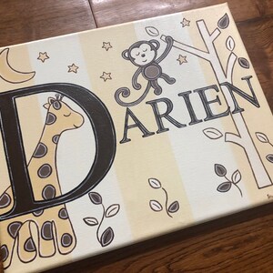 May include: A canvas painting with a yellow and white striped background. The letter "D" is painted in black with a giraffe inside. The name "Darien" is written in black letters. A monkey is hanging from a tree branch with leaves. The painting has a whimsical, nursery theme.