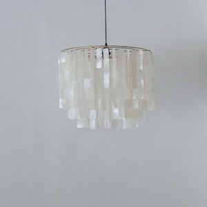 May include: A white, hanging pendant light with a gold-colored metal frame. The light fixture is adorned with numerous rectangular, translucent shell pieces, creating a layered, cascading effect. The light hangs from a black cord.