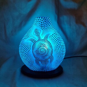 Pode incluir: Um difusor elétrico de óleos essenciais azul com um design de tartaruga. O difusor tem formato de gota e é coberto por pequenos orifícios espaçados. O design da tartaruga é visível no centro. Mede cerca de 20 cm de altura.