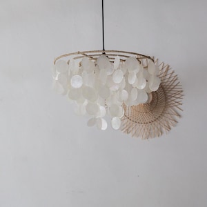 May include: A hanging pendant light fitting featuring multiple tiers of circular, translucent white capiz shell discs suspended from a circular frame wrapped in natural tan jute cord, with a thin black electrical cord extending upwards.