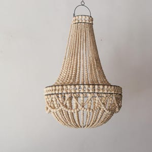 Op de afbeelding: Een grote, houten kralen kroonluchter met een metalen frame. De kralen zijn van nature gekleurd en creëren een cascade-effect.