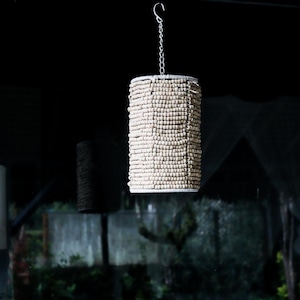 Peut inclure: Un luminaire suspendu en perles blanches suspendu à une chaîne argentée. Les perles sont disposées en forme cylindrique, créant un design unique et moderne.