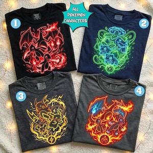 May include: Four short-sleeved t-shirts featuring neon-style graphic prints of various characters. The black shirt shows red fire-breathing creatures, the navy shirt displays green plant-like figures, the grey shirt depicts yellow electric creatures, and the charcoal shirt features orange fire-breathing creatures. A teal star-shaped sign with the text ALL POKEMON CHARACTERS is centred at the top.