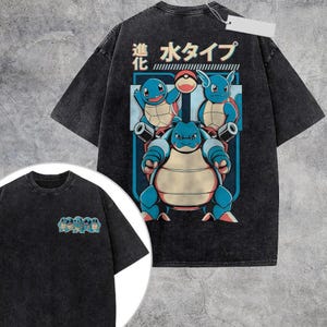 May include: A charcoal gray acid-wash t-shirt featuring a large back graphic of three blue turtle-like creatures and a red and white ball. The Japanese text reads "Evolution" and "Water Type." A smaller version of the creatures is on the front left chest.