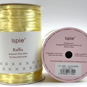 May include: A spool of bright yellow Ispie raffia yarn made from 100% viscose plant fiber. The label indicates a length of 250 meters, a crochet hook size of 2.5-4mm, and the color name Shiny Canary, lot number 031026042, color code 205A.