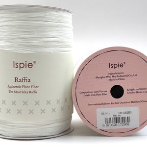 May include: A spool of white Ispie raffia yarn made from 100% viscose plant fiber. The label reads Ispie Raffia Authentic Plant Fiber The Most Silky Raffia. The side of the spool indicates a length of 250 meters and a crochet hook size of 2.5-4mm.