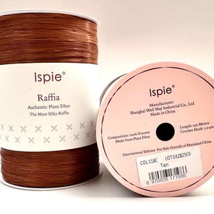 May include: Two spools of tan raffia ribbon. The label on the spool reads "Ispie Raffia, Authentic Plant Fiber, The Most Silky Raffia." The second spool shows the manufacturer, Shanghai Well May Industrial Co., Ltd, and the length is 250 meters.