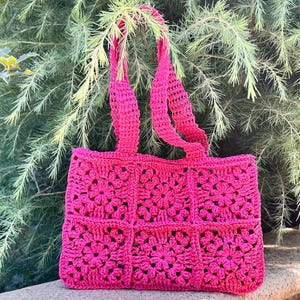 May include: A bright fuchsia crochet tote bag constructed from six square granny motifs arranged in two rows of three. The bag features two matching fuchsia crochet handles and a textured, open-work floral pattern throughout the entire surface.