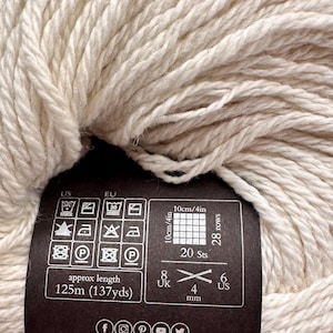 May include: A skein of off-white yarn with a black paper label. The label displays care instructions, a gauge of 20 stitches and 28 rows for a 4-inch square, a length of 137 yards, and a 4 mm needle size. The text knitrowan.com is printed at the bottom.