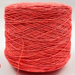 May include: A spool of bright coral colored yarn with a subtle shimmer. The yarn is wound tightly and has a smooth texture.