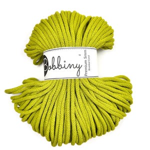 May include: A skein of bright green braided cord. The cord is wrapped and held together with a white label that reads "Bobbiny Premium 5mm Braided Cord". The cord is a vibrant, solid color, and the texture is visible.