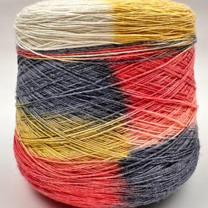 Pode incluir: Uma bola de fio com um padrão degradê multicolorido. O fio é branco, amarelo, cinza e rosa.