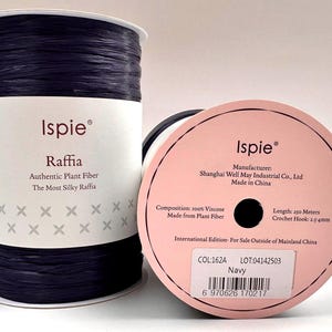 May include: Two navy blue raffia spools. The text on the label reads "Ispie Raffia, Authentic Plant Fiber, The Most Silky Raffia." The pink label on the spool reads "Length: 250 meters, Crochet Hook: 2.54mm."