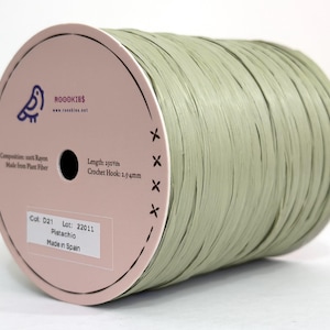 May include: A spool of light green raffia yarn made from 100% rayon plant fibre. The spool features a pink circular side label with the text ROOOKIES, 250 Yds, and Crochet Hook: 2.5-4mm. A white sticker displays Col: D21, Lot: 22011, Pistachio, Made in Spain.
