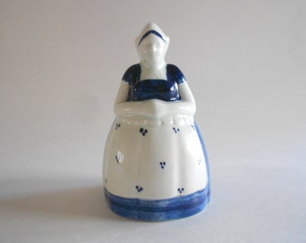 Może przedstawiać: Biała ceramiczna figurka kobiety w niebiesko-białej sukience i niebiesko-białym kapeluszu. Figurka jest ozdobiona niebieskimi kropkami.