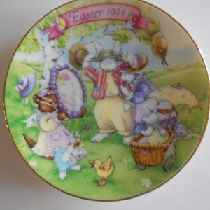Pode incluir: Um prato de porcelana com uma borda dourada apresentando uma ilustra&ccedil;&atilde;o colorida de coelhos e outras criaturas da floresta. O prato tem o texto "Easter 1994" nele.