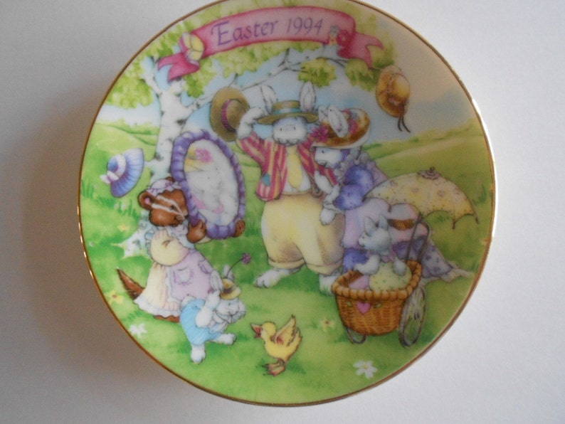 Pode incluir: Um prato de porcelana com uma borda dourada apresentando uma ilustra&ccedil;&atilde;o colorida de coelhos e outras criaturas da floresta. O prato tem o texto "Easter 1994" nele.